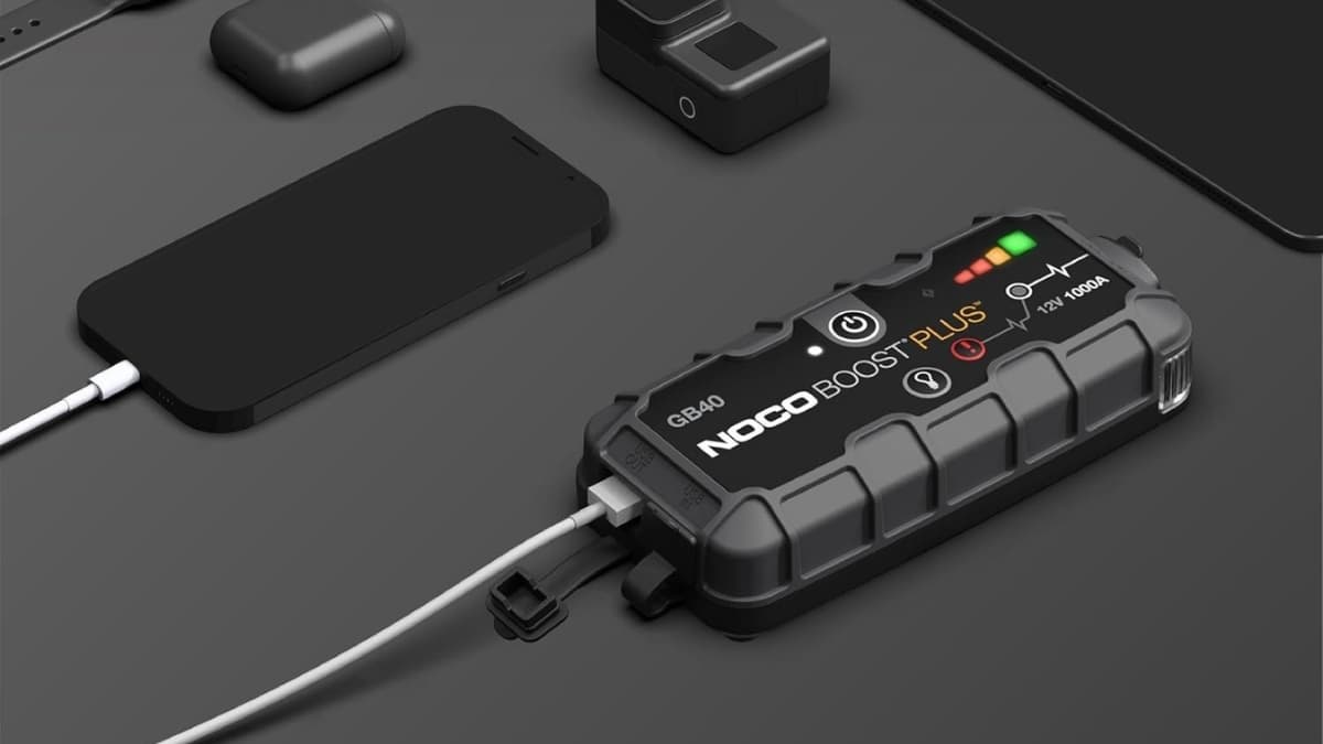 NOCO Boost GB40 jump starter charging a phone with other small devices on a dark surface.