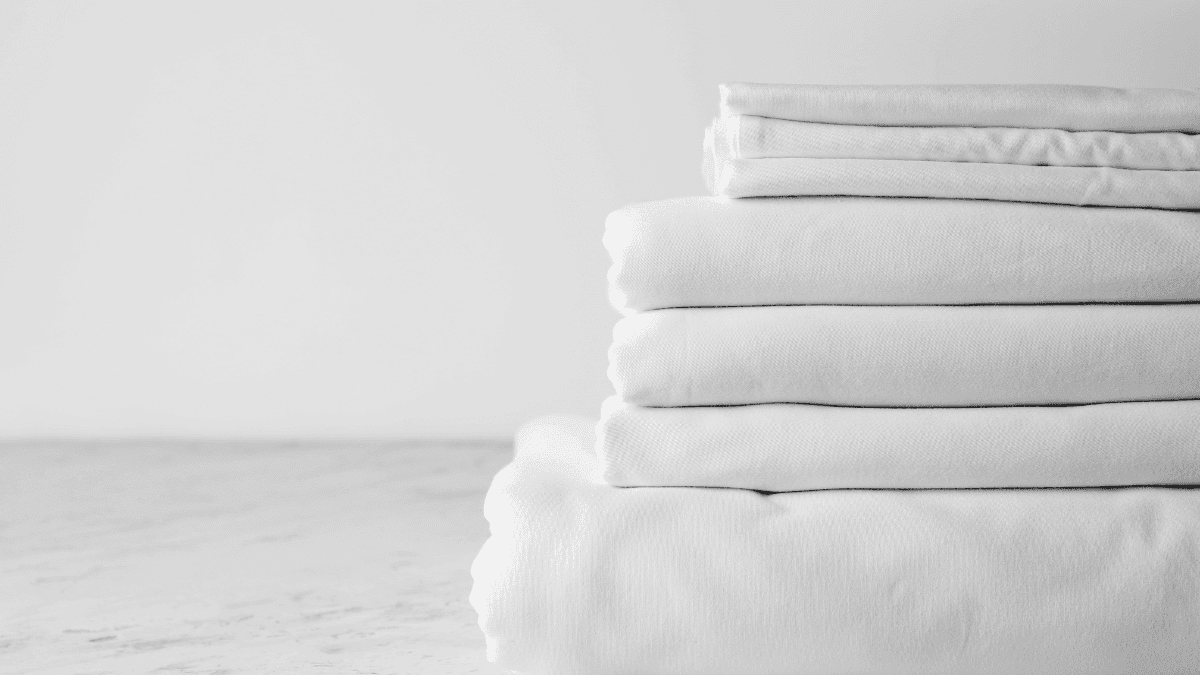 Neatly folded white premium bed sheets stacked on a clean surface, highlighting soft fabric texture and fresh bedding.